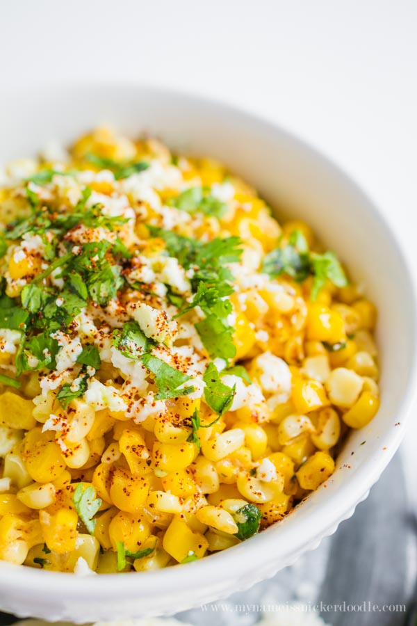 Grilled corn in a white bowl with cheese and cilantro on top.