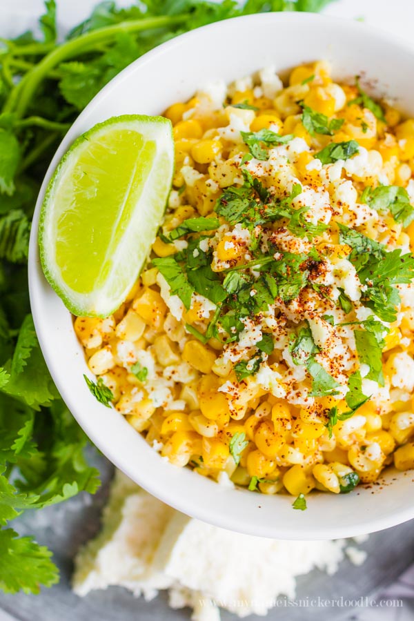 A white bowl full of grilled corn topped with cheese and chopped cilantro.