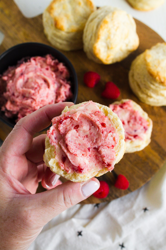 A hand holding a biscuit slathered with raspberry butter.