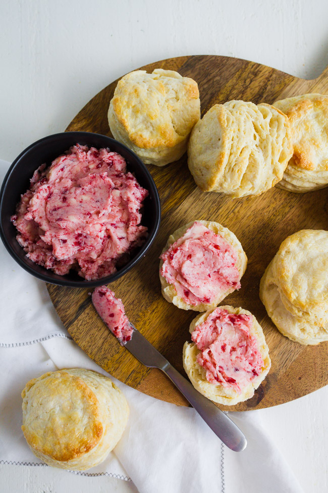 Raspberry butter slathered on top of homemade biscuits with a butter knife on a wood cutting board