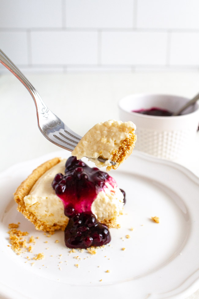 A fork taking a bite of a no bake cheesecake with blueberry topping.  