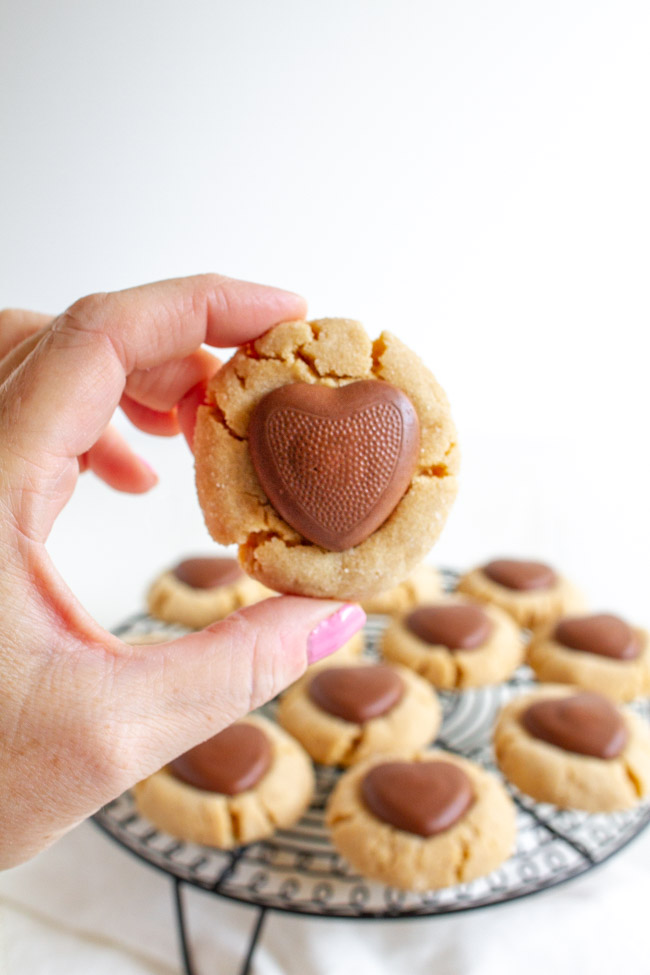 A hand holding a Peanut Butter cookie with a chocolate heart