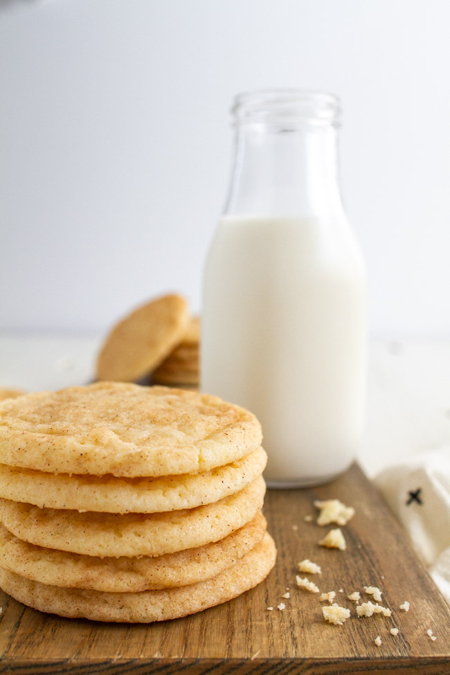 Stacked up Snickerdoodles on a wood tray with a glass of milk.