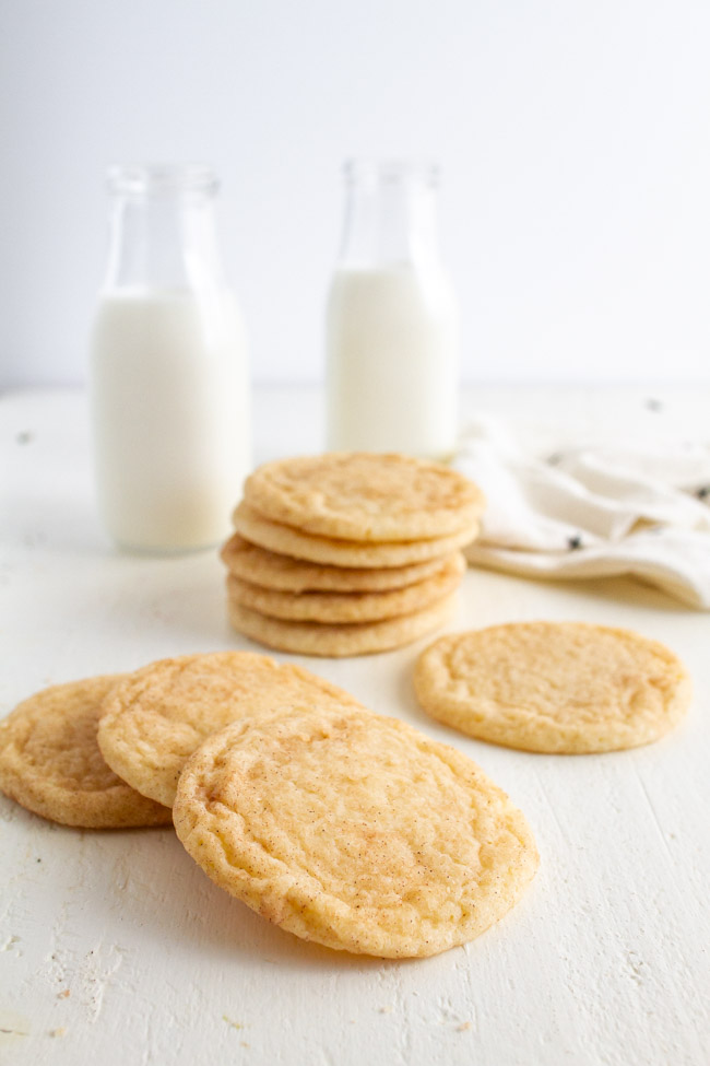 Stacked up Snickerdoodle Cookies on a white table with two glasses of milk. 