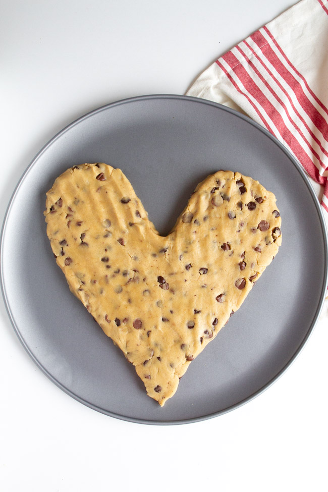 Heart shaped chocolate chip cookie dough on a silver pizza pan.