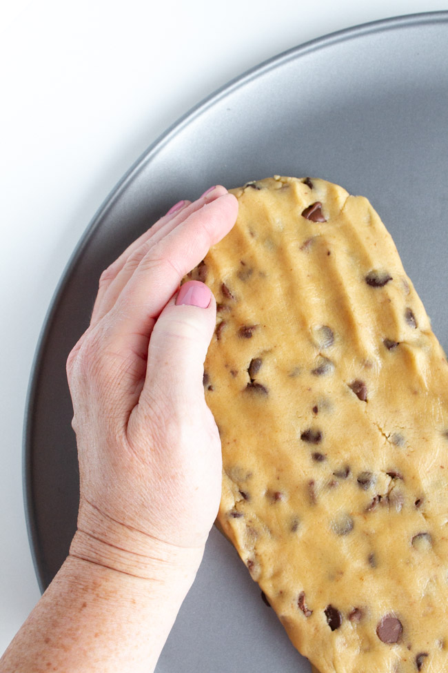 A hand shaping chocolate chip cookie dough into a heart.