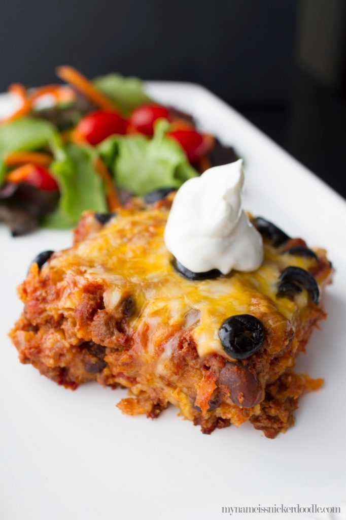 A serving of Beef Enchilada Casserole with a dollop of sour cream on top on a white plate. 