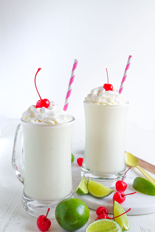 Two glass mugs full of Frozen Key Lime beverage topped with whipped cream and cherries.