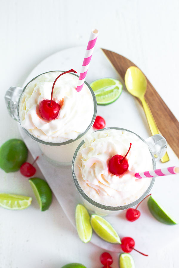 Two glass mugs full of Frozen Key Lime beverage on a marble board with limes and cherries.