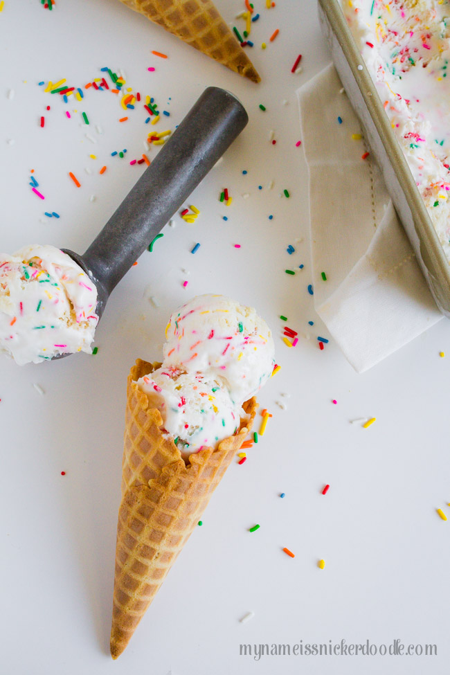 A waffle cone with two scoops of sprinkle ice cream laying on a white table. 