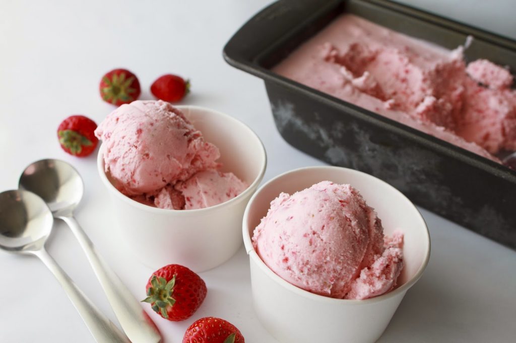 Two white bowls with strawberry ice cream and two spoons.