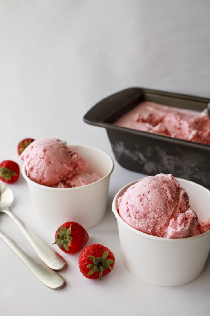 Two white paper bowls with strawberry ice cream on a white table.