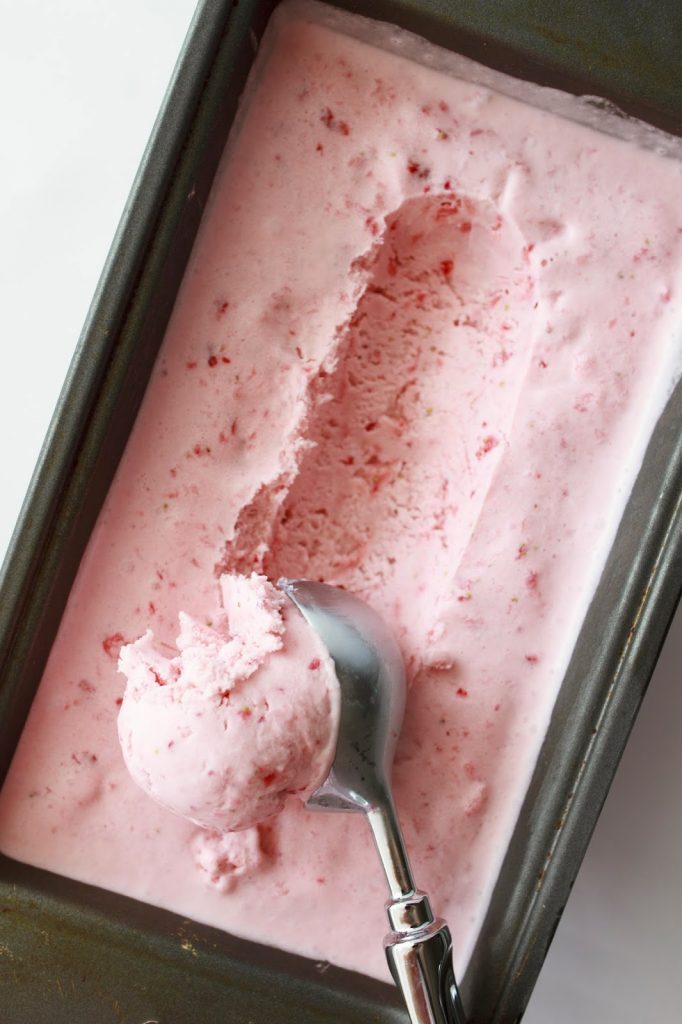 A container full of Strawberry Ice Cream with a scoop taken out of it.  