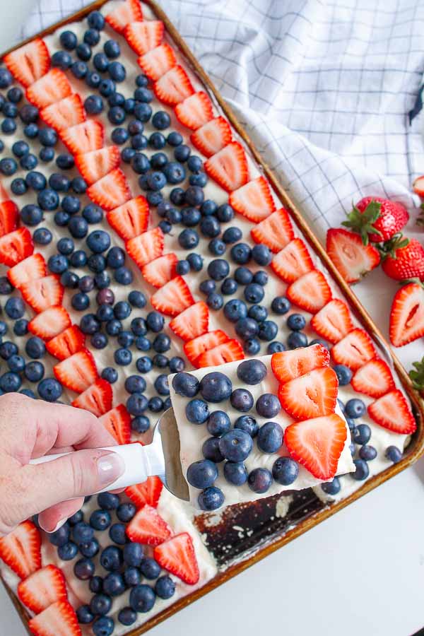 Patriotic Fruit Pizza with strawberries and blueberries in a cookie sheet on a white table.