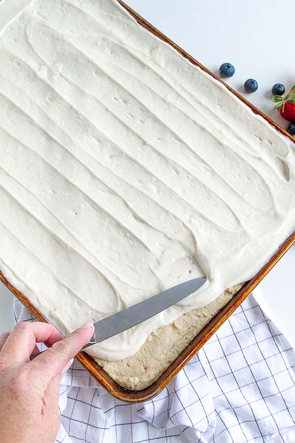 A butter knife spreading frosting on top of a sugar cookie crust.  