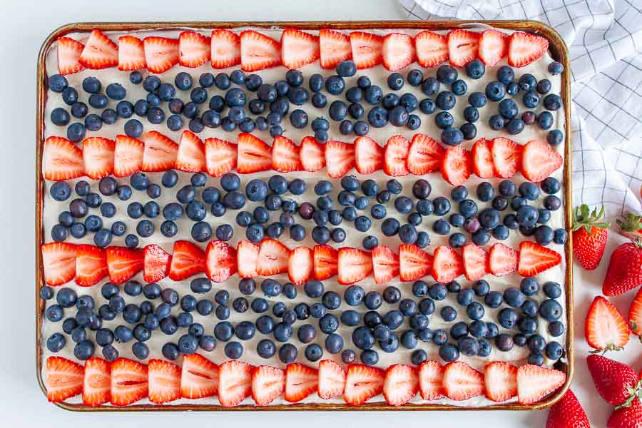 Sliced Strawberries and blueberries on a sheet pan of frosted sugar cookie crust.  