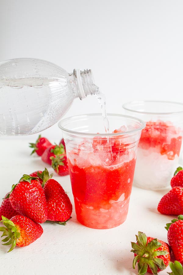 Club soda being poured into a cup with strawberry puree.