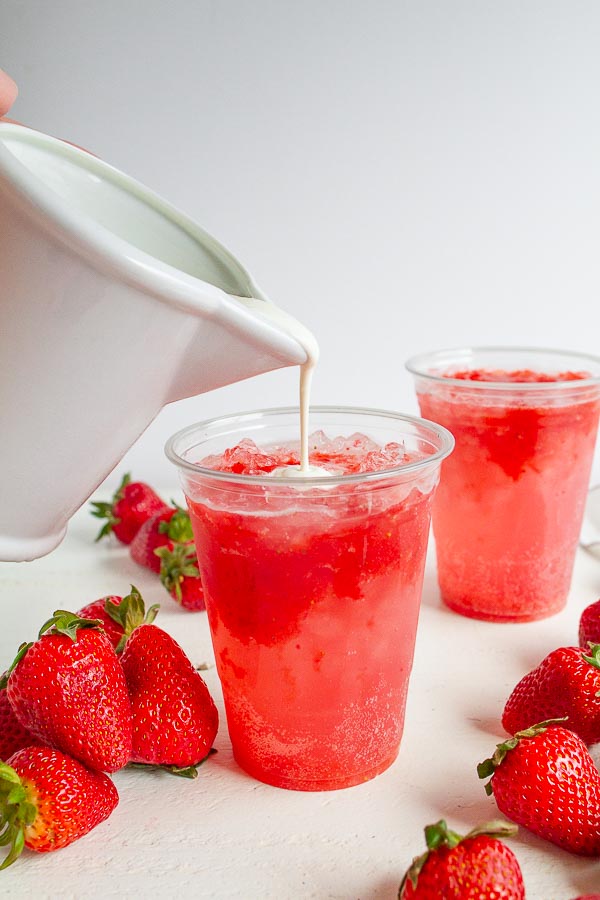 Heavy cream being poured into a cup of strawberry soda.
