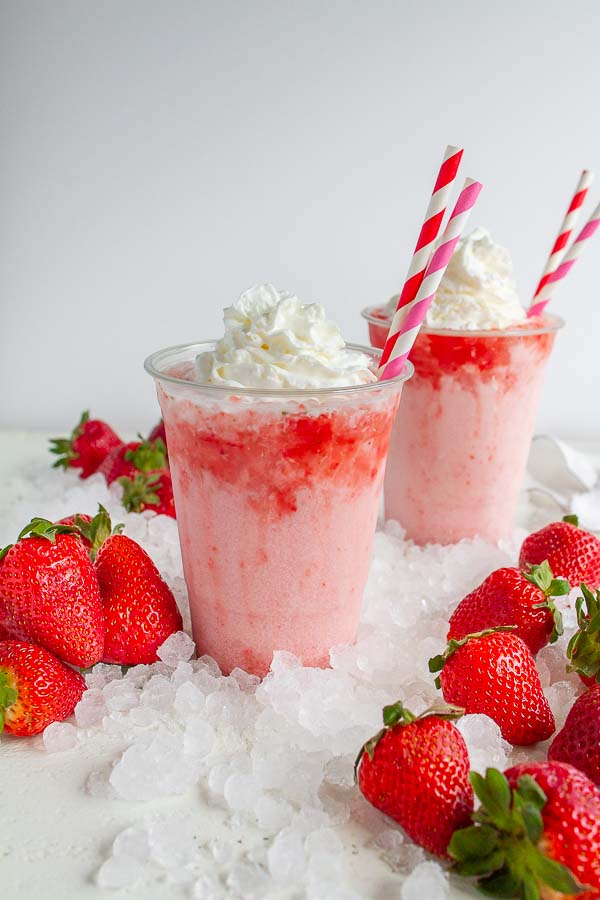 Two clear cups with strawberry soda and ice in it.  