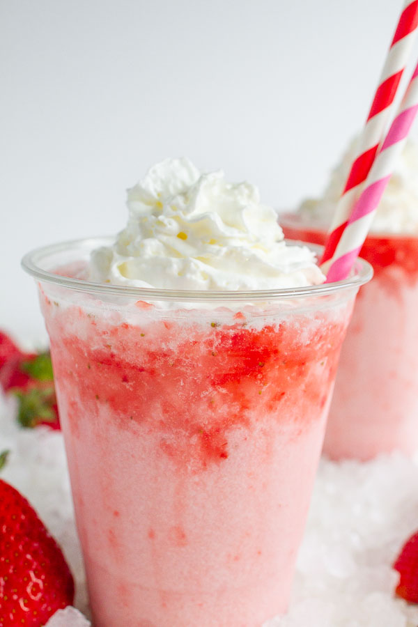 Two clear cups with strawberry soda topped with whipped cream.