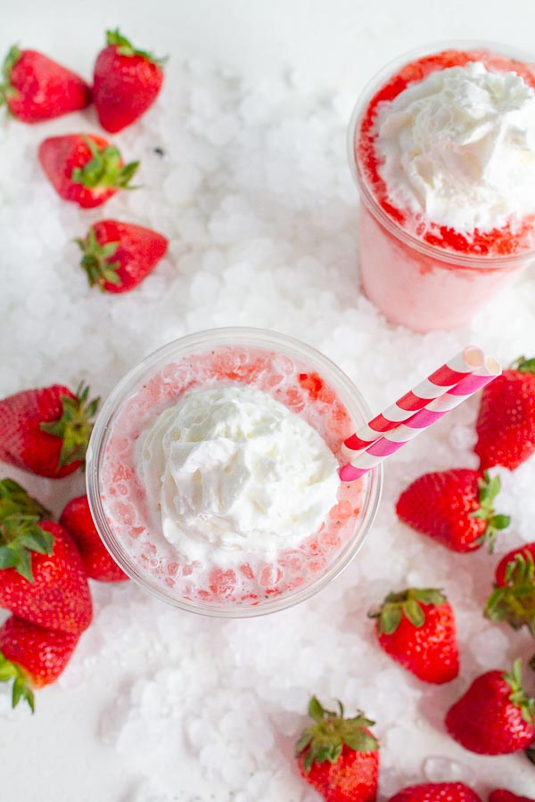 Two clear cups with strawberry soda topped with whipped cream.