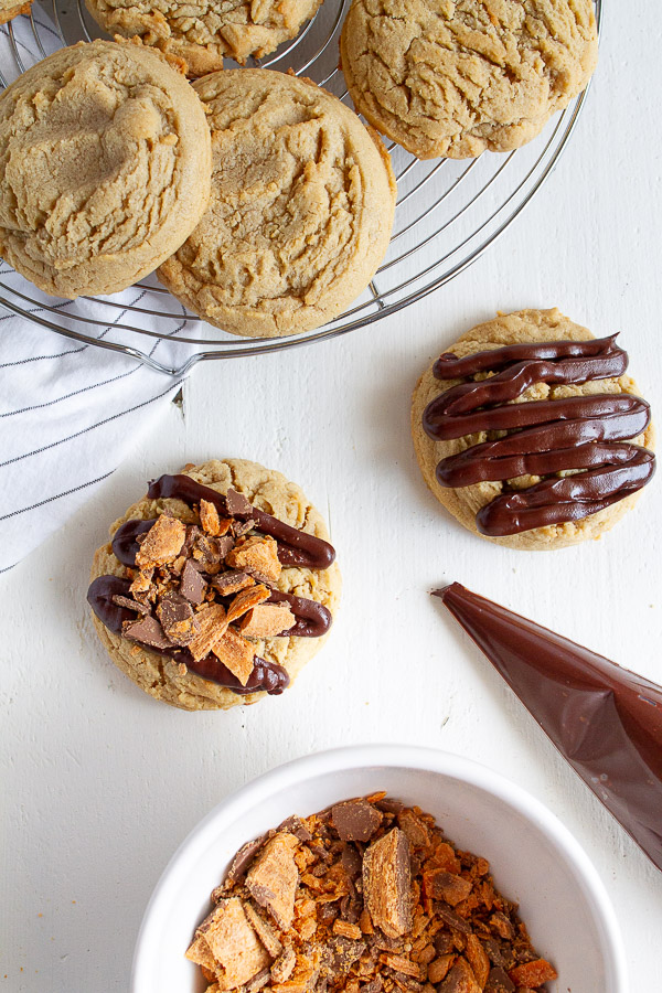 Butterfinger Peanut Butter Cookies are made with a tender chewy peanut butter cookie, drizzled with chocolate and topped with crushed Butterfinger candy!  