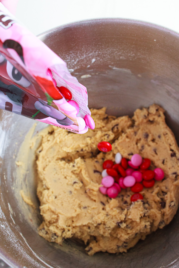 Pink and Red M&M's being added to chocolate chip cookie dough.