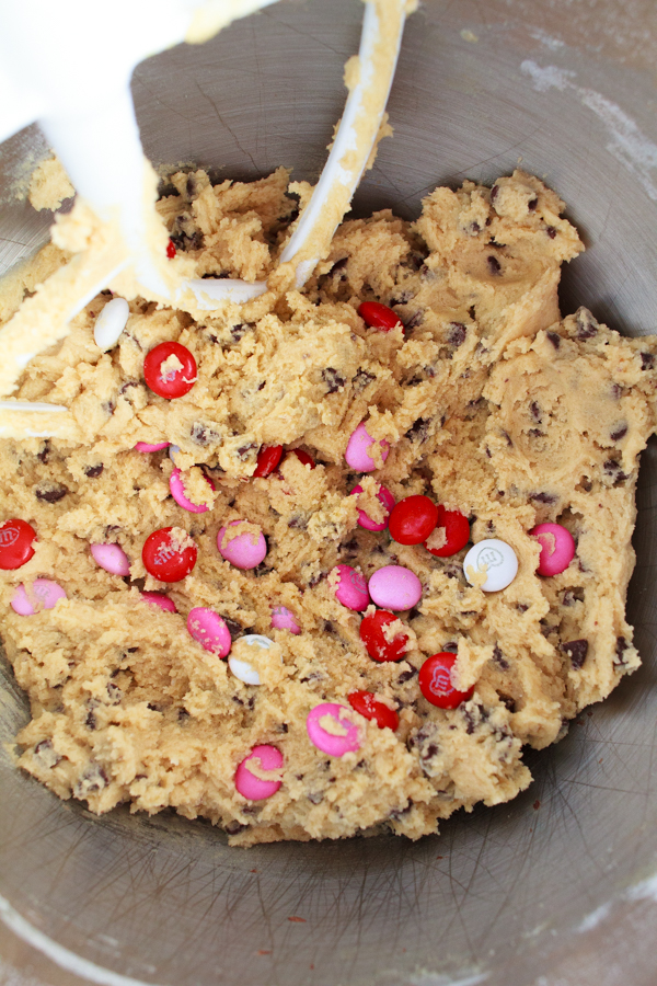 Pink and Red M&M's being added to chocolate chip cookie dough.