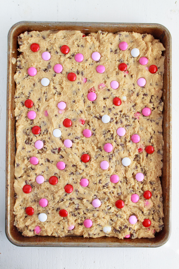 Pink and Red M&M's being added to chocolate chip cookie dough.