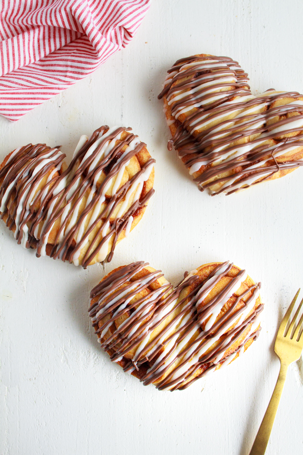 Heart Shaped Cinnamon Rolls are drizzled with Cream Cheese Frosting and Chocolate.