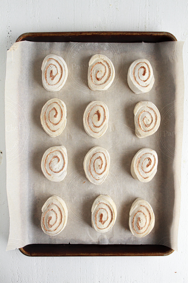 Thawing out cinnamon rolls on a parchment lined baking sheet.