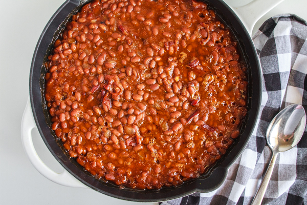 Baked Beans in a black cast iron skillet with a checked napkin.