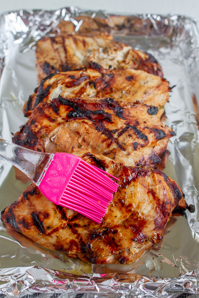 A pink silicone basting brush on top of grilled chicken.