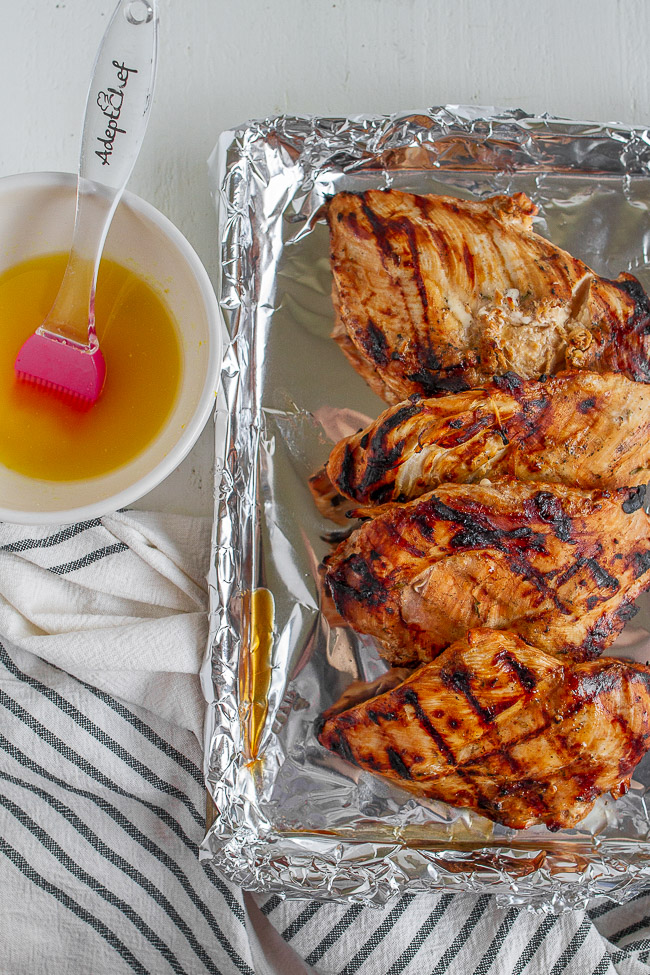 Grilled lemon chicken on a foil lined pan along side a bowl of lemon butter.