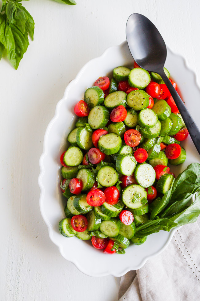 Tomatoes and cucumbers along with fresh basil sliced and tossed in a white dish.