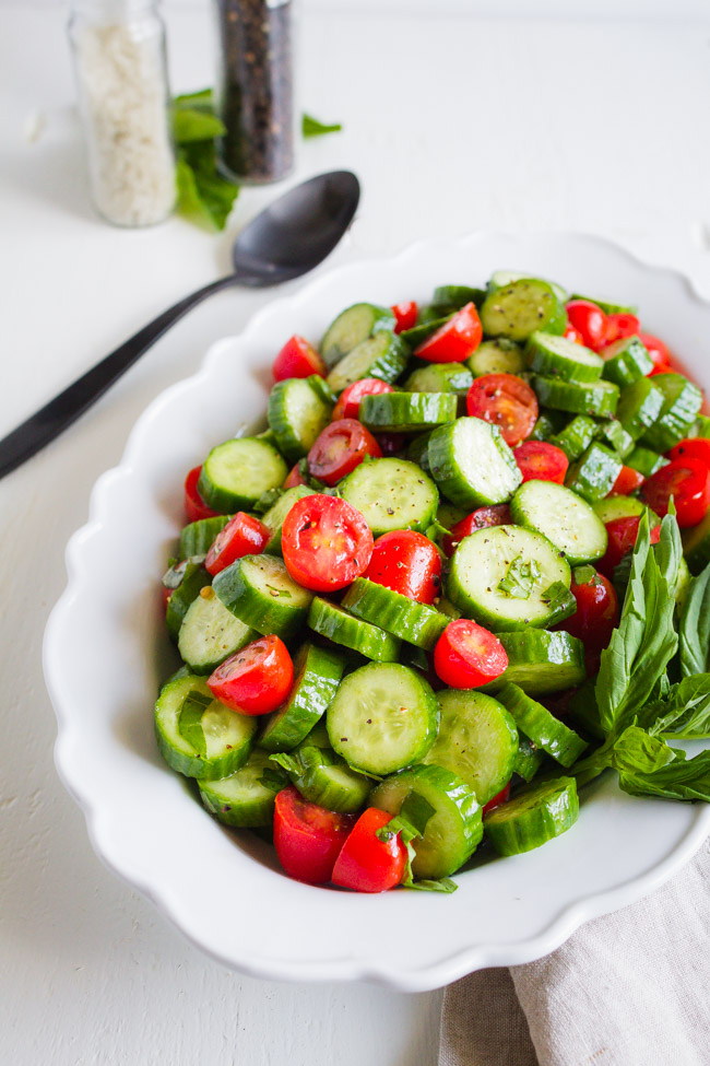 Basil, tomatoes and cucumbers sliced and tossed in a white dish.