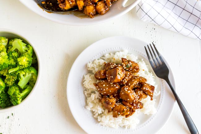 A white plate with rice and sesame chicken.