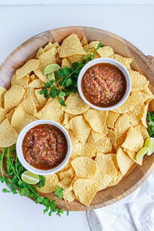 Two bowls of salsa on a wooden tray with tortilla chips.