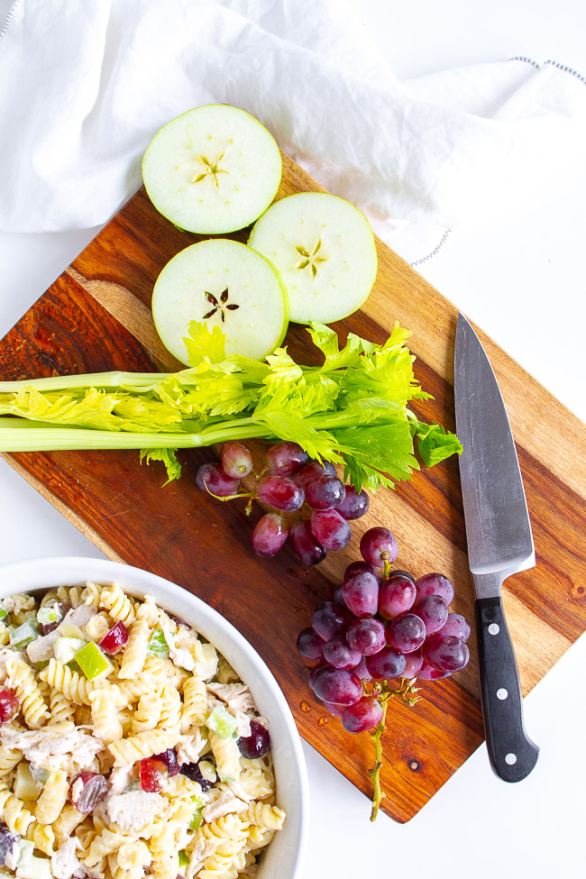 Celery, green apples and purple grapes on a wooden cutting board.