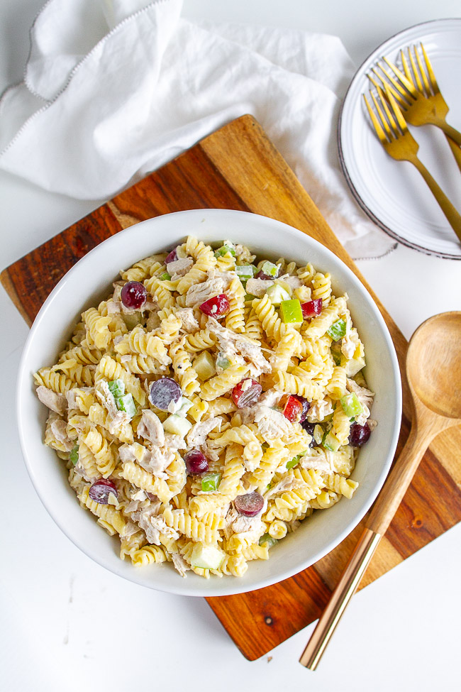 A white bowl with Chicken Pasta Salad sitting on a wooden cutting board.