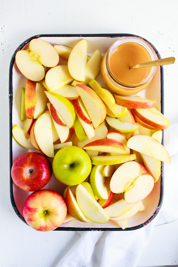 A white platter of sliced apples with a jar of caramel sauce