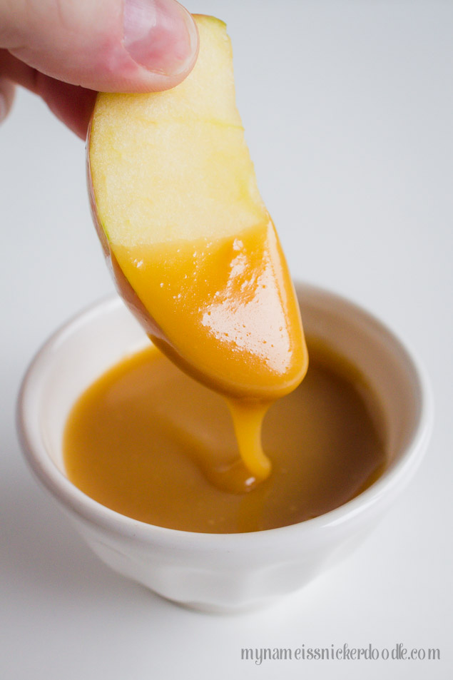 A sliced apple being dipped into a homemade caramel sauce.