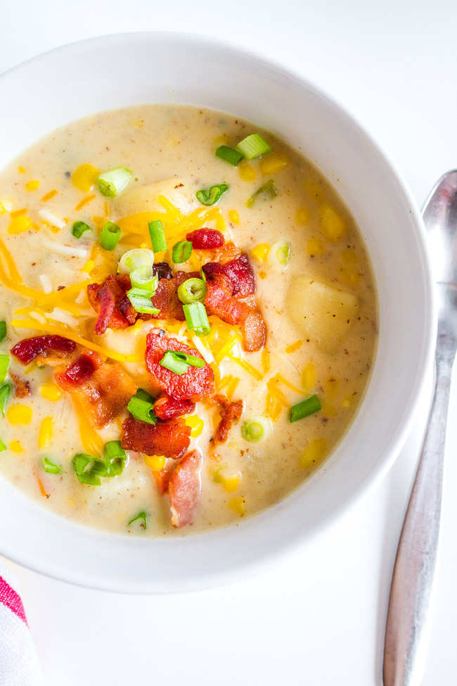 White bowl full of Corn Chowder topped with bacon and shredded cheese.