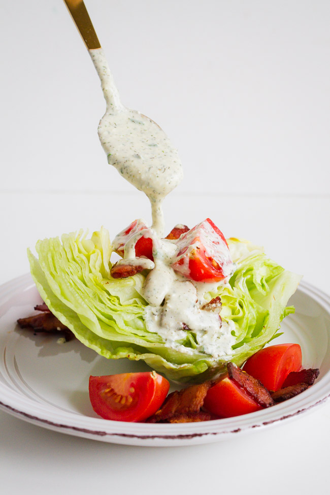 A wedge salad being topped with Homemade Ranch Dressing.  