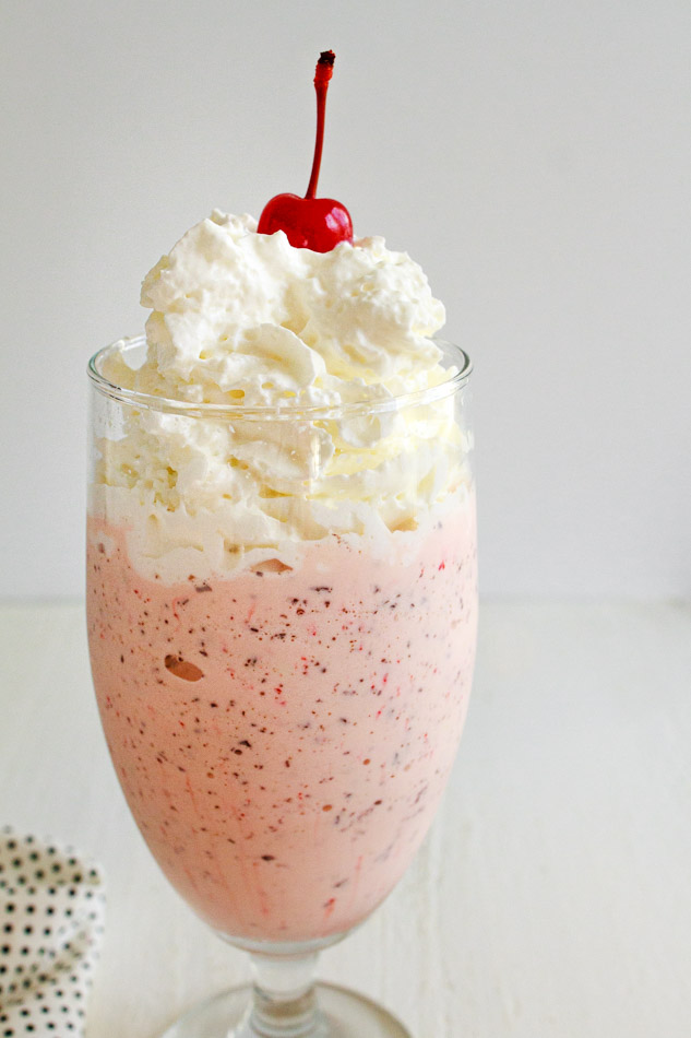 Copy cat recipe for Chickfila's Peppermint Chip Milkshake in a big glass cup topped with whipped cream and a cherry.  