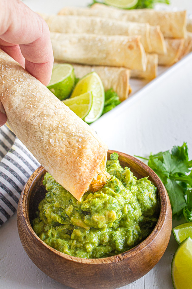 Taquitos recipe being dipped into guacamole.